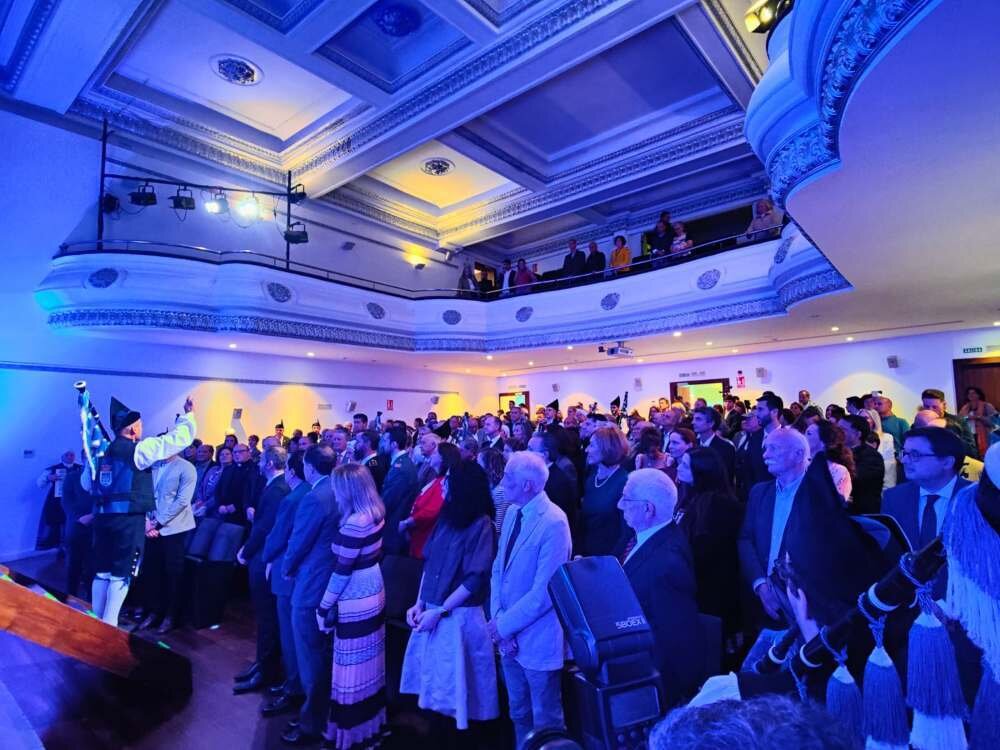 Los asistentes de pie mientras la Real Banda de Gaitas Ciudad de Oviedo interpreta el himno de Asturias.